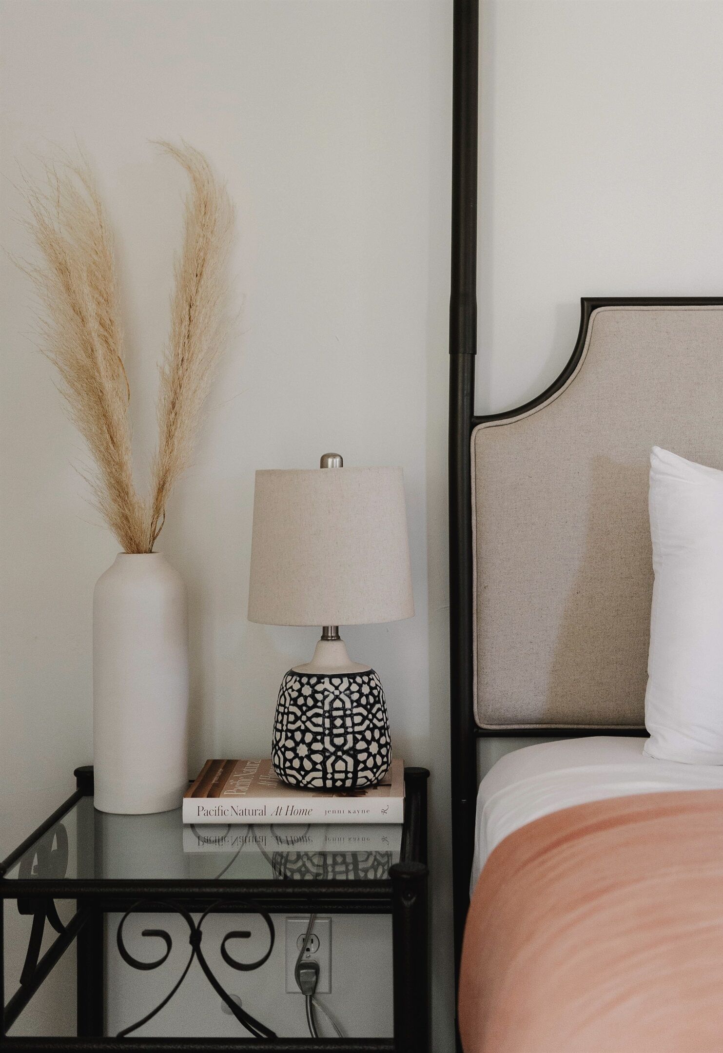 A neatly arranged bedroom with a bed, bedside table, lamp, and decorative vase.