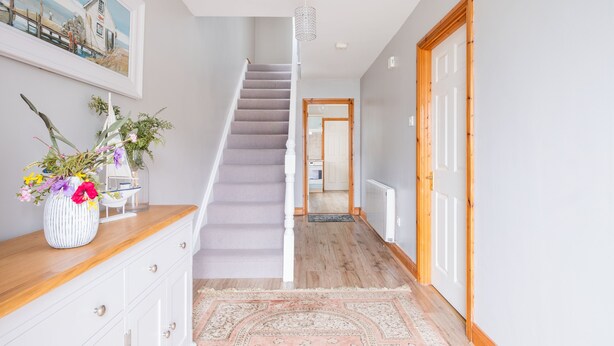 A hallway with a wooden floor, a staircase, a white door, and a framed painting on the wall. - Summercove 04 - Family Estate (Lahinch)