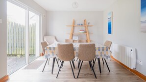 A dining area with a table set for four, chairs, a wooden ladder shelf, and a view through large windows. - Summercove 04 - Family Estate (Lahinch)