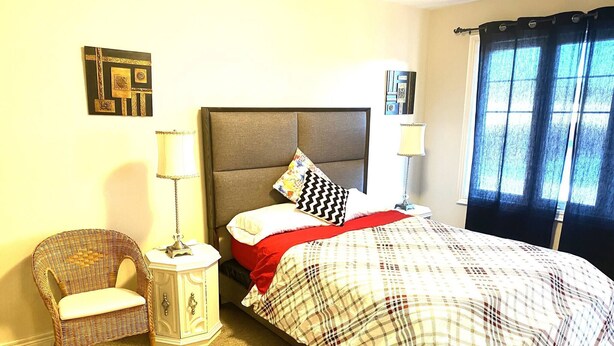 A bedroom with a bed, a chair, a nightstand, and a window with curtains. - Niagara Sleeps 6 Cozy 3bed 3bath Near Falls (Thorold)