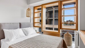 Un dormitorio con una cama grande, una lámpara colgante y vistas a un edificio a través de una ventana.