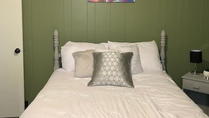 Une chambre à coucher avec un lit, des oreillers, une table de chevet et une œuvre d’art murale.
