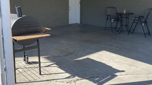 Un espace extérieur abrité comprenant un barbecue, deux tables avec des chaises et une porte.