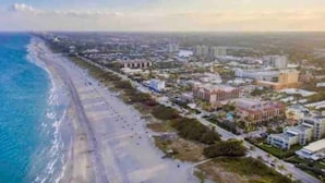 An aerial view of a coastal city with a long beach, dense urban area, and various buildings.