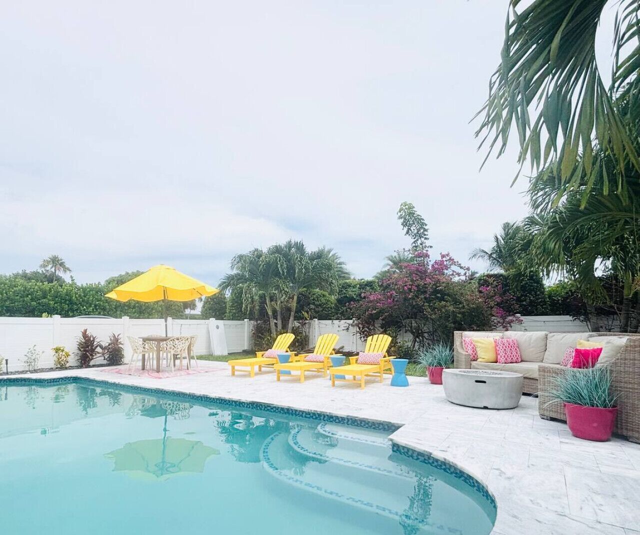 A swimming pool with yellow lounge chairs and a white outdoor sofa with pink cushions.