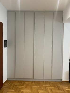 A room with a large wardrobe, wooden flooring, and a door on the left.