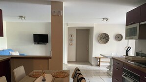 A modern kitchen with a dining area, featuring a wooden table with woven placemats, a built-in oven, and a flat-screen TV mounted on the wall. - 8-person villa in quiet location near lake and beach (Saint-Paul-en-Forêt)