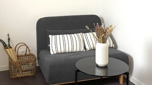 Ein Wohnzimmer mit einem grauen Sofa, zwei gerahmten Motivationssprüchen, einem kleinen runden Tisch und einer Vase mit Trockenblumen.