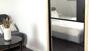 Ein Zimmer mit einem Bett, einem kleinen Tisch mit einer Vase und einem Bilderrahmen an der Wand.