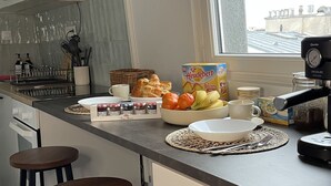Eine moderne Küche mit weißen Schränken, einem großen Fenster und einer Frühstücksecke mit Brot, Früchten und einer Kaffeemaschine.