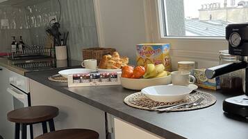 A modern kitchen with white cabinets, a large window, and a breakfast setup including bread, fruits, and a coffee maker.