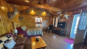 A cabin interior with a wooden ceiling, mounted animal heads, a bed, a sofa, a TV, and a fireplace. - The Cozy Den (Wellington)