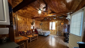 A cabin with a wooden interior, a bed, a dining area, and a kitchen. - The Cozy Den (Wellington)