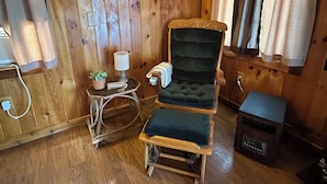 A wooden cabin interior with a cushioned chair, a small table with a lamp, and a fish-shaped wall decoration. - The Cozy Den (Wellington)