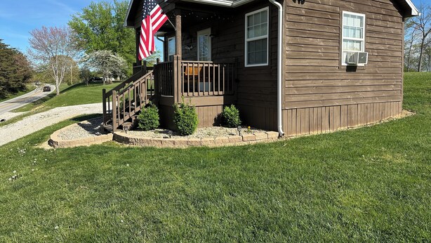 A small wooden cabin with a porch, an American flag, and a small garden. - The Cozy Den (Wellington)