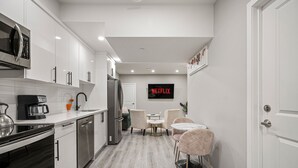 Una cocina moderna con armarios blancos, electrodomésticos de acero inoxidable y un comedor con una mesa y sillas.