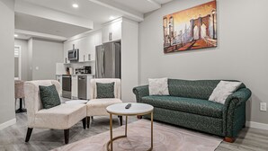 Una sala de estar moderna con un sofá verde, dos sillones, una mesa de centro y un cuadro de un puente en la pared.