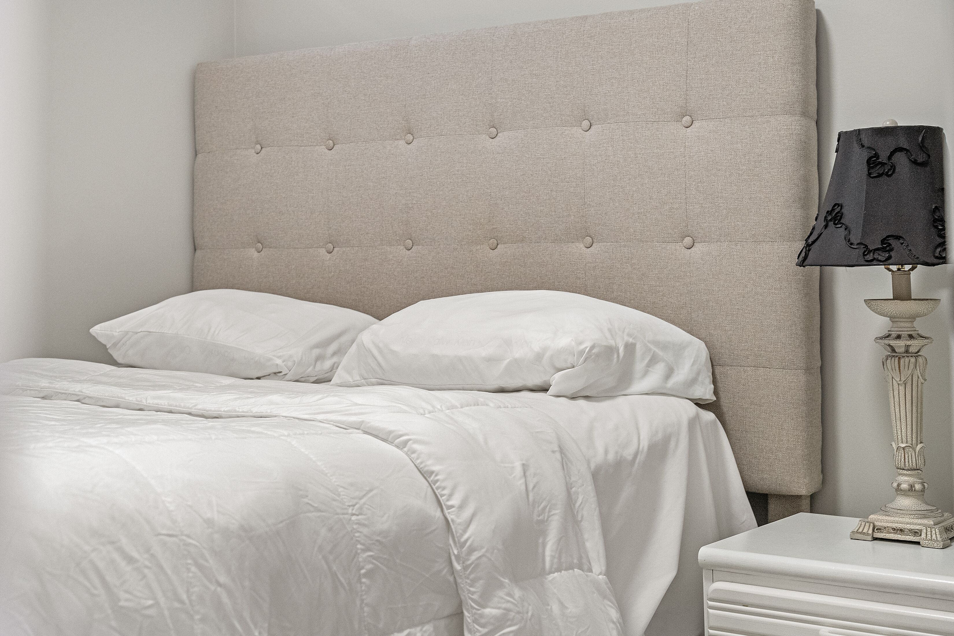 A neatly made bed with a tufted headboard, white bedding, and a bedside table with a lamp.