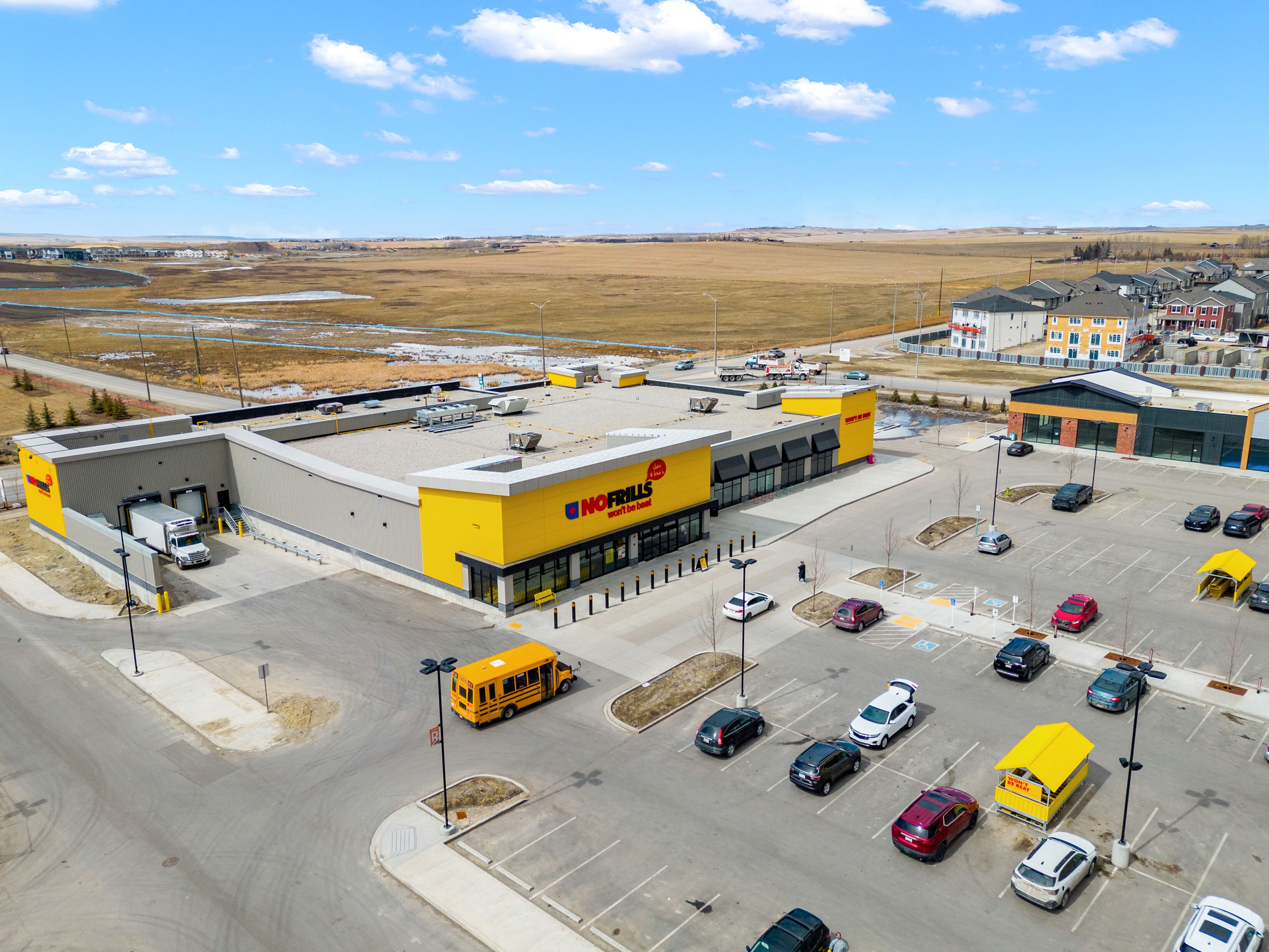 A large parking lot with multiple vehicles, including a school bus, and a building with a prominent yellow and red sign.