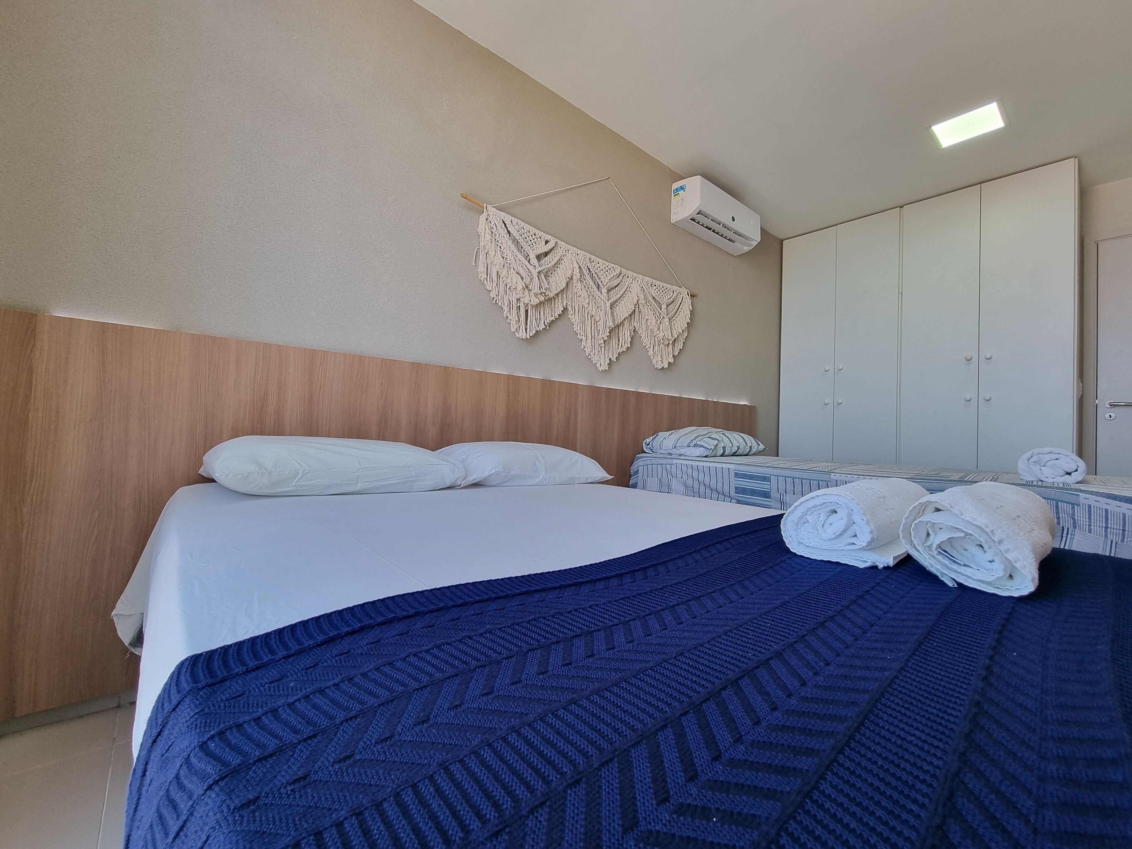Une chambre d’hôtel comprenant un lit, une tête de lit en bois, un climatiseur fixé au mur, un grand miroir et une armoire.