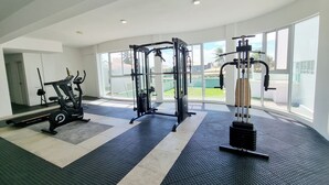 A gym with cardio machines, weightlifting equipment, and large windows offering a view of the outdoors. - Vista Mar, Piscina e Lazer no Areias do Mar (Barra de São Miguel)