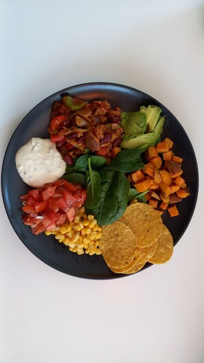 A plate with a variety of foods including rice, beans, avocado, corn, spinach, tomatoes, and tortilla chips. - Forest Family Home (Ytterhogdal)