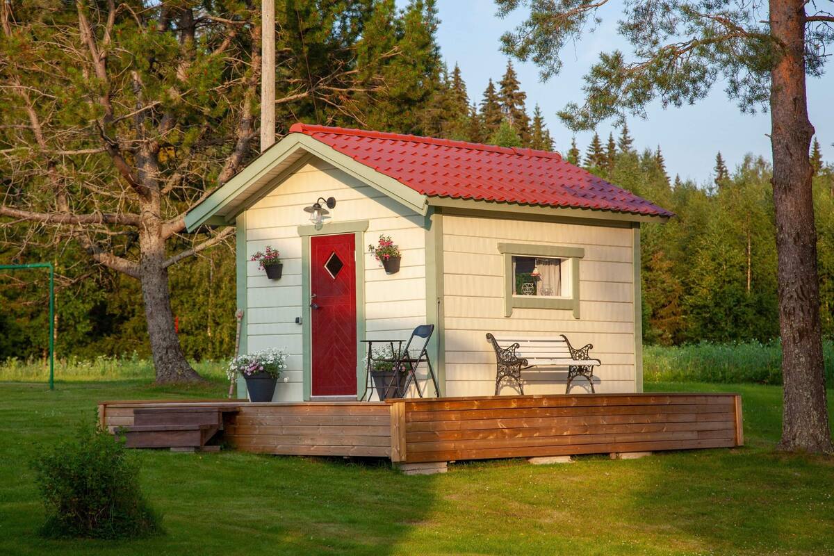 A small cabin with a red door, a window, and a porch with benches.