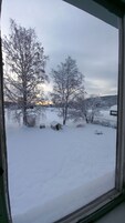Paisagem nevada com árvores secas e uma pequena cabana.