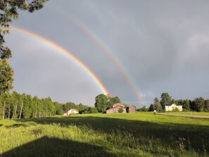 A rural landscape with a rainbow, green fields, and wooden buildings. - Forest Family Home (Ytterhogdal)
