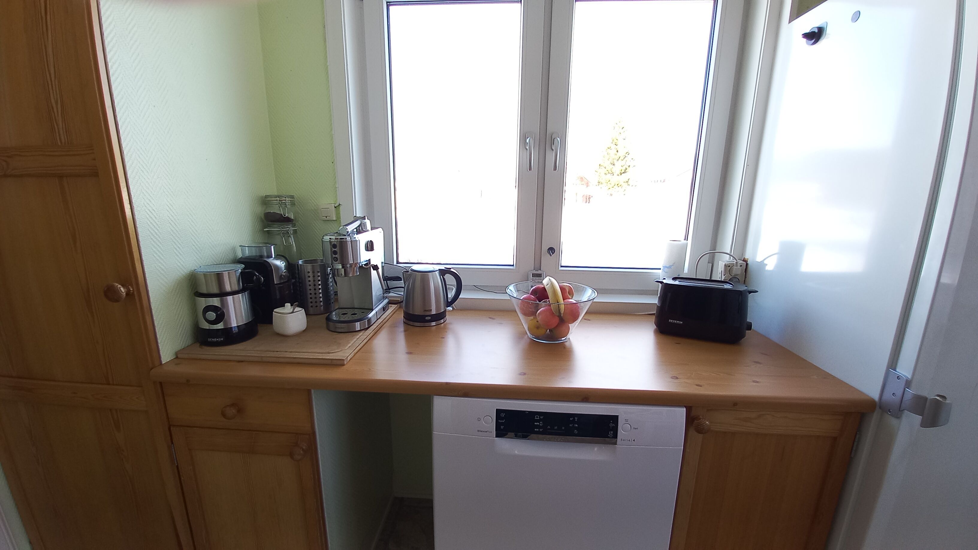 A kitchen with a dishwasher, a coffee maker, a toaster, and a bowl of fruit on the counter.