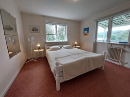 Quarto com uma cama, duas mesas de cabeceira com luminárias, um ventilador, um radiador e uma janela com vista para árvores.