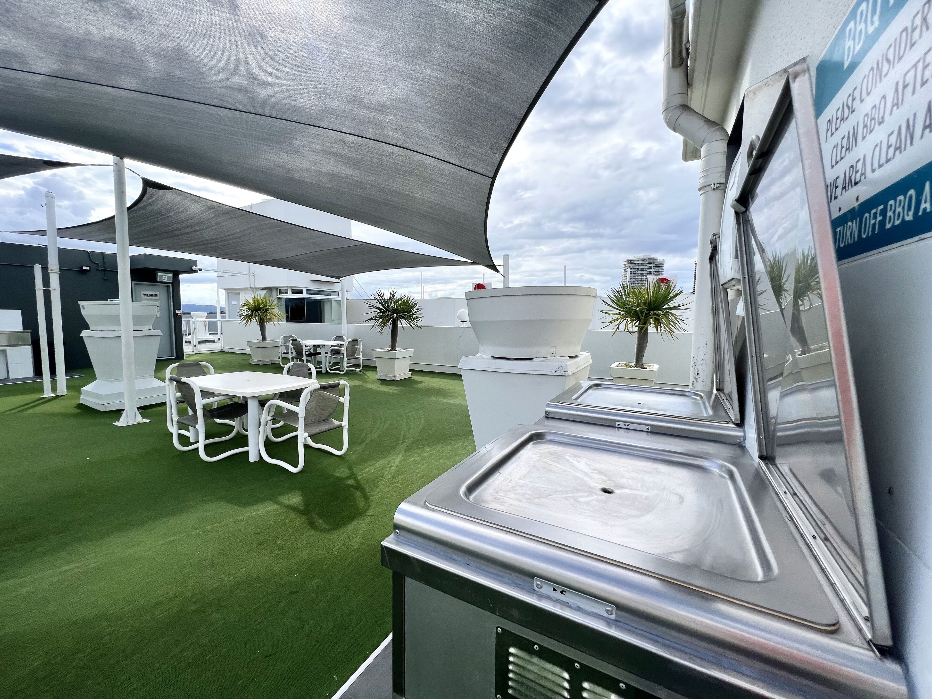 An outdoor patio area with a BBQ station, seating, and planters.