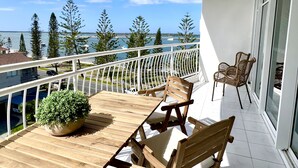 A balcony with a wooden table and chairs, a potted plant, and a view of the sea and trees. - Ocean View 2BR Apartment w/hot tub. Heated pool, Games room, Gym (Biggera Waters)