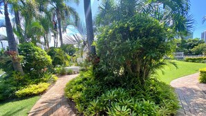 A landscaped garden with a curved brick pathway, various shrubs, and tall palm trees. - Ocean View 2BR Apartment w/hot tub. Heated pool, Games room, Gym (Biggera Waters)