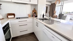 A modern kitchen with white cabinets, a stainless steel sink, and a dishwasher. - Ocean View 2BR Apartment w/hot tub. Heated pool, Games room, Gym (Biggera Waters)