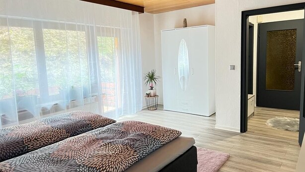 Ein modernes Zimmer mit einem großen Bett, einem Kleiderschrank und einer Tür zu einem weiteren Raum.