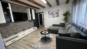 Ein modernes Wohnzimmer mit Steinrückwand, einem Flachbildfernseher, einem grauen Sofa und einem kleinen runden Couchtisch.