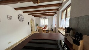 Eine großzügige Küche mit Kochinsel, Holzbalken an der Decke, einem Essbereich im Hintergrund und einem Messerblock auf der Arbeitsfläche.