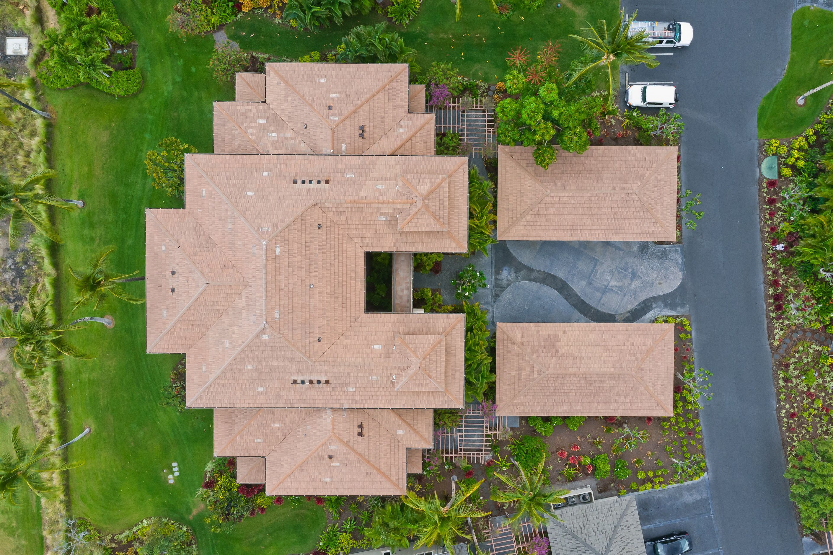 Un grand bâtiment doté de plusieurs sections de toit, entouré de jardins bien entretenus et de palmiers.