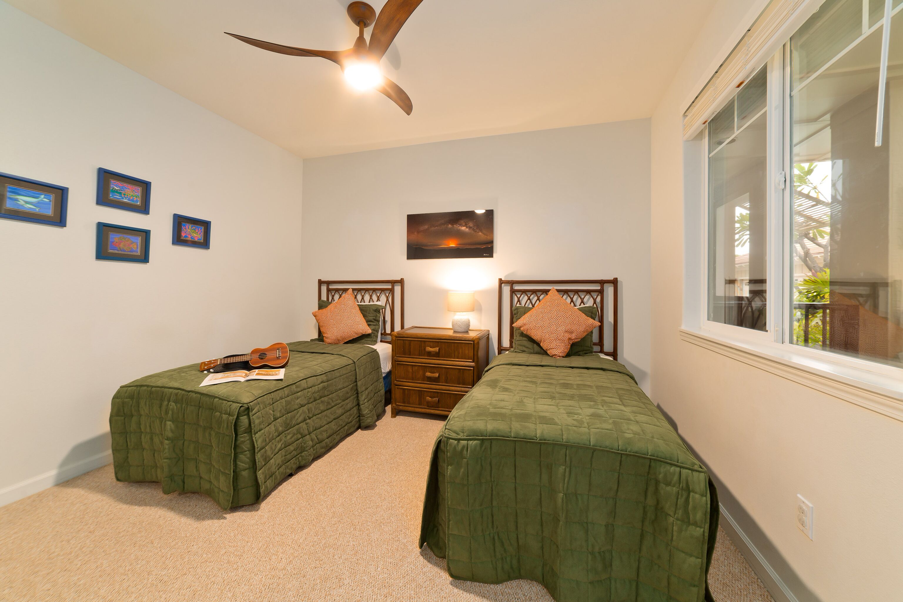A bedroom with two single beds, a ceiling fan, a nightstand with a lamp, and framed pictures on the wall.