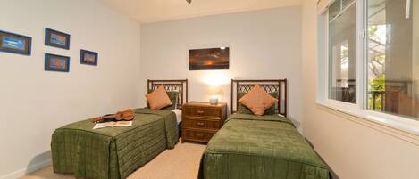 A bedroom with two single beds, a ceiling fan, a nightstand with a lamp, and framed pictures on the wall.