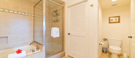 A bathroom with a glass-enclosed shower, a bathtub with a red flower, a toilet, and a framed picture on the wall.
