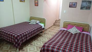 Two single beds with red and black checkered bedding, a small bedside table, and a wall-mounted light switch.