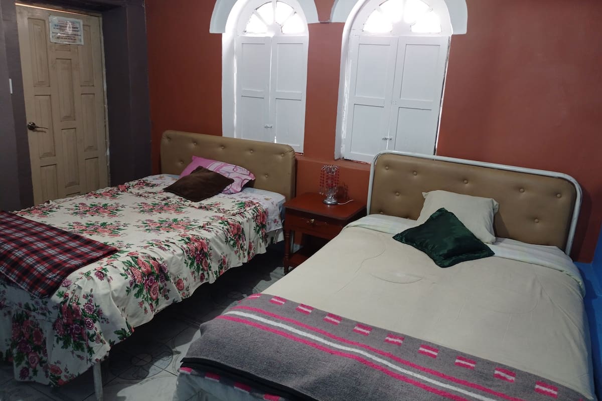 Une chambre avec deux lits simples, une porte en bois et deux fenêtres en arc de cercle.