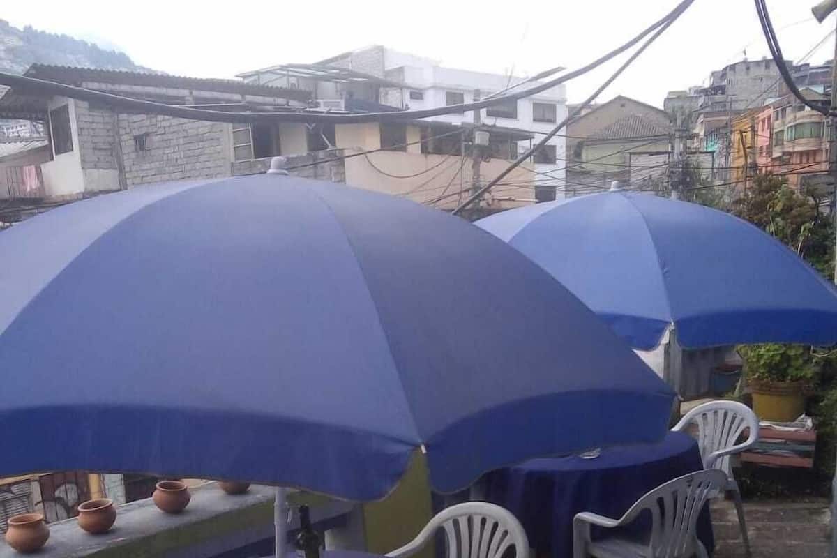 Espace extérieur aménagé avec des parasols bleus, des chaises en plastique blanches et une table décorée de poteries.