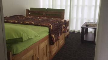 A bedroom with a wooden bed, a small table with a remote, and a TV mounted on the wall.