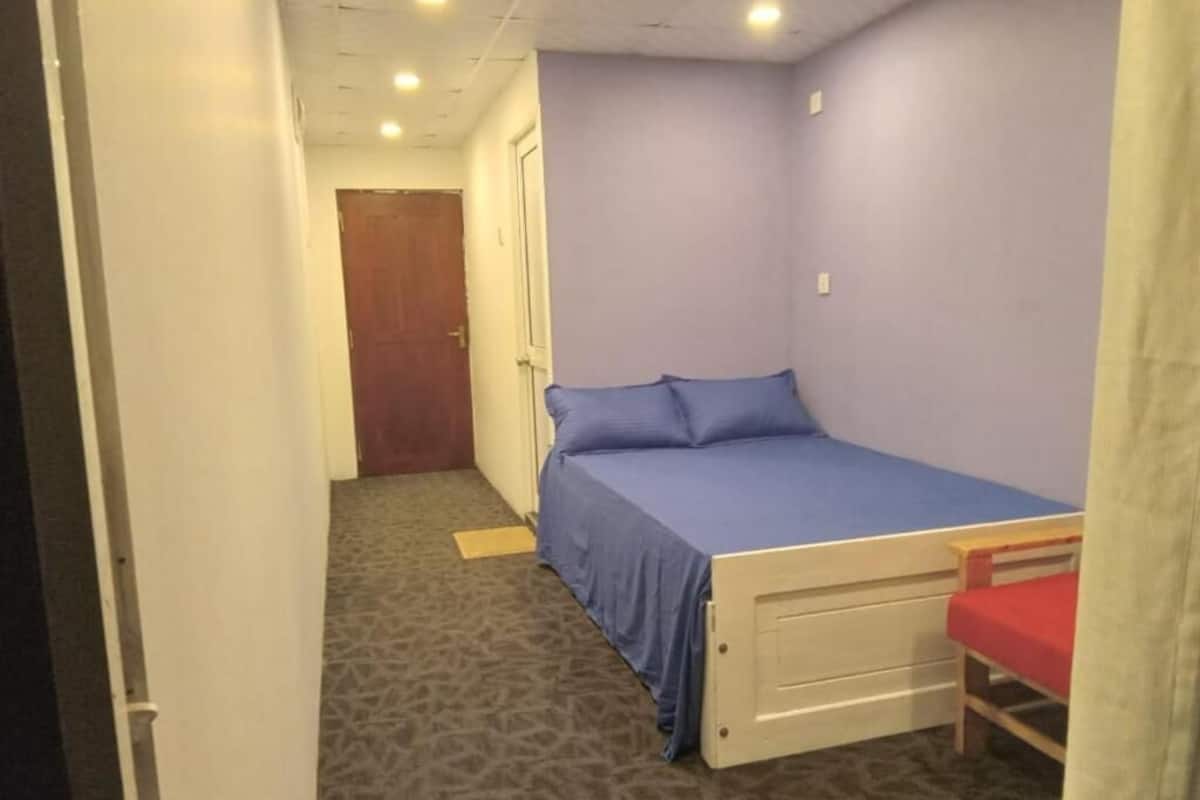 A small bedroom with a single bed, a wooden nightstand, and a red chair.