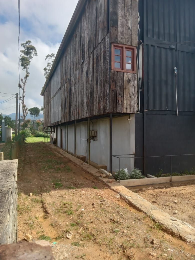 Un bâtiment doté d’une grande fenêtre et d’une porte, entouré d’un chemin de terre et de quelques plantes.