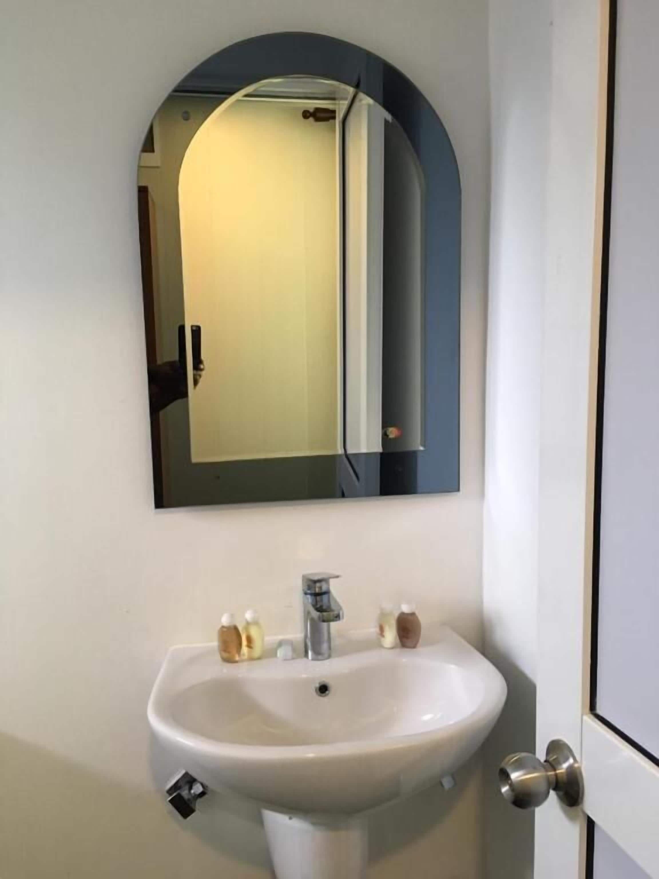 Een badkamer met een wit wastafel, een spiegel en een deur.