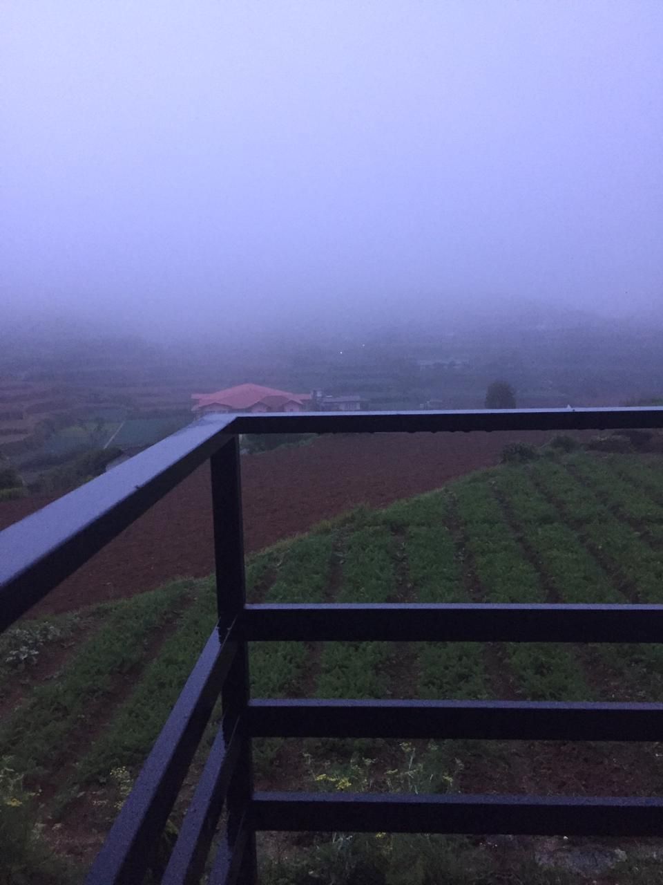 A foggy landscape with a red-roofed building in the distance, viewed from a balcony with a black railing.